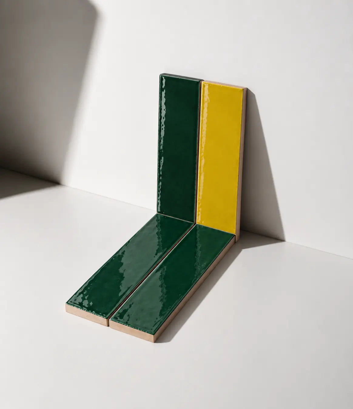 Glossy Citron Yellow and Forest Green handmade ceramic tiles arranged against a white wall in natural sunlight.