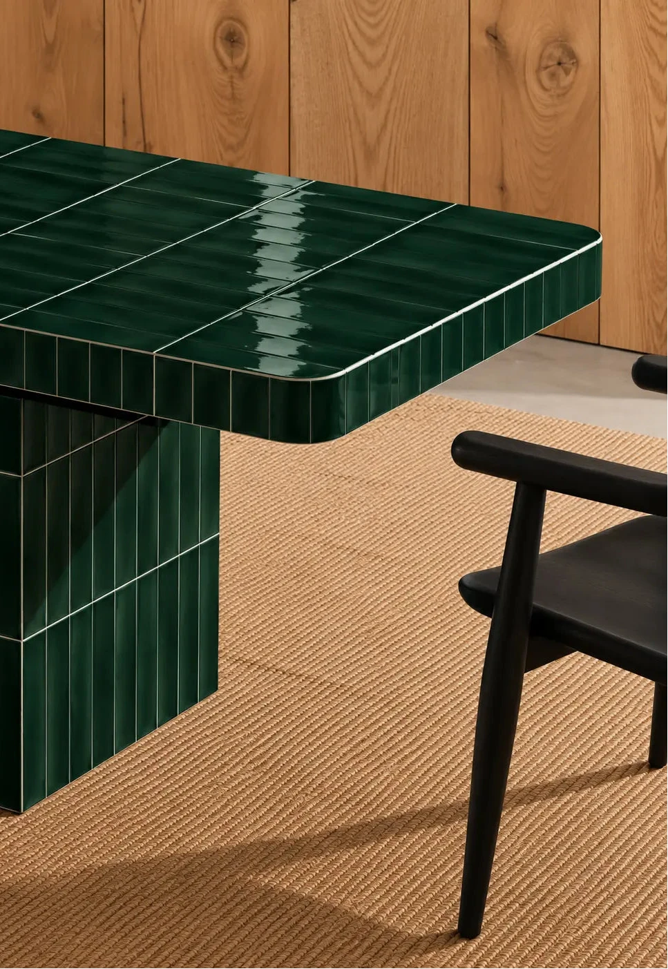
Glossy forest green rectangular ceramic tiles covering a dining table, paired with a dark wood chair and natural woven rug.