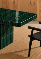 
Glossy forest green rectangular ceramic tiles covering a dining table, paired with a dark wood chair and natural woven rug.
