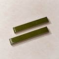 Two glossy olive green rectangular ceramic tiles with a textured matte finish, displayed diagonally on a light beige textured background.