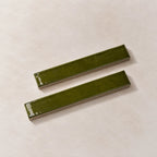 Two glossy olive green rectangular ceramic tiles with a textured matte finish, displayed diagonally on a light beige textured background.