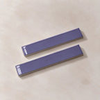 Two glossy lilac rectangular ceramic tiles with a textured beige base, arranged diagonally on a light beige textured surface.