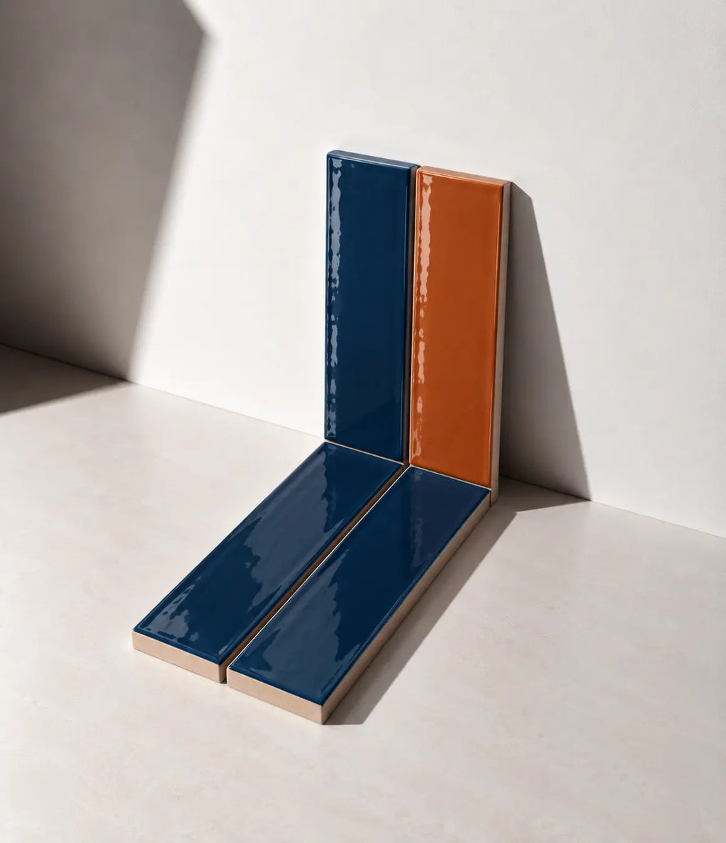 Glossy terracotta orange and marine blue handmade ceramic tiles arranged against a white wall in natural sunlight.