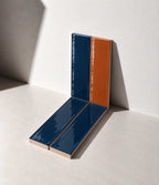 Glossy terracotta orange and marine blue handmade ceramic tiles arranged against a white wall in natural sunlight.
