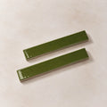 Two glossy olive green rectangular ceramic tiles with a slight bevelled edge, displayed diagonally on a textured beige background.
