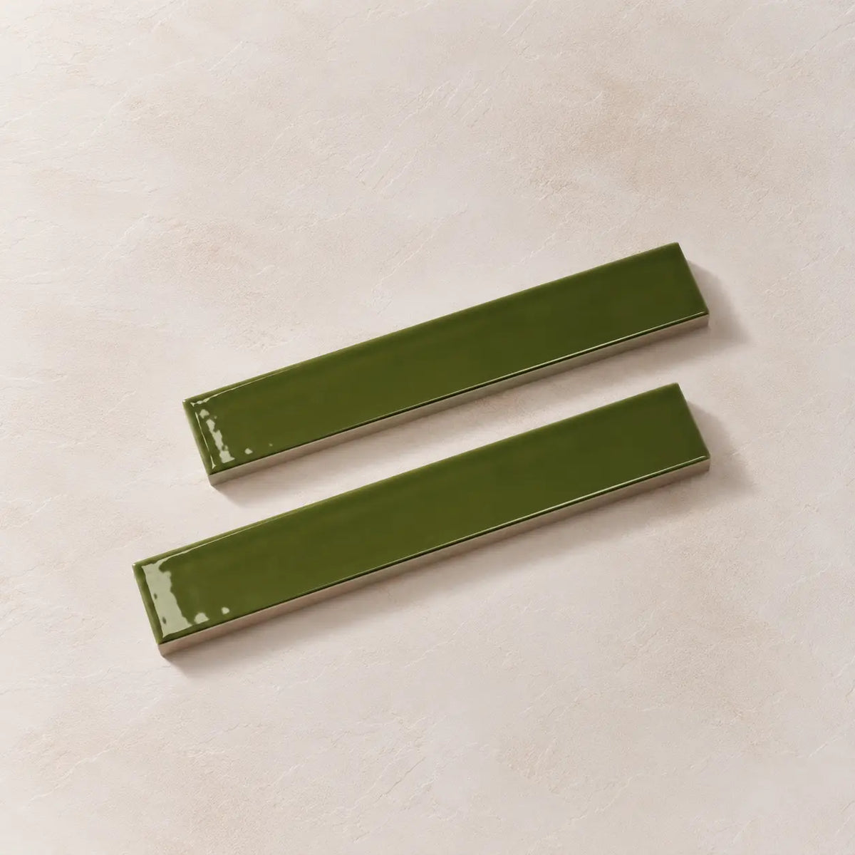 Two glossy olive green rectangular ceramic tiles with a slight bevelled edge, displayed diagonally on a textured beige background.