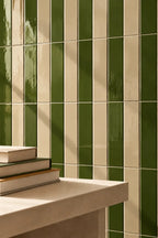 Vertical green and cream striped glossy ceramic wall tiles with a light stone countertop and stacked books in the foreground.