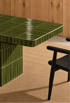 
Glossy olive green rectangular ceramic tiles covering a dining table, paired with a dark wood chair and natural woven rug.