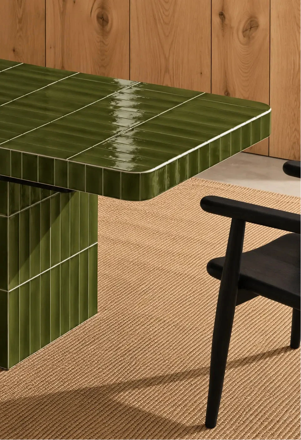 
Glossy olive green rectangular ceramic tiles covering a dining table, paired with a dark wood chair and natural woven rug.
