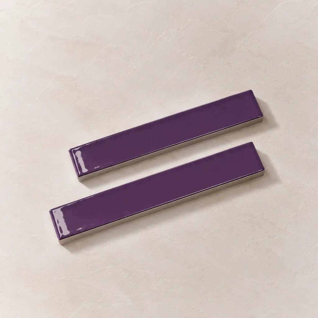 Two glossy purple rectangular ceramic tiles with silver metallic edges, displayed diagonally on a light beige textured background.