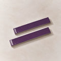 Two glossy purple rectangular ceramic tiles with silver metallic edges, displayed diagonally on a light beige textured background.