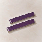 Two glossy purple rectangular ceramic tiles with silver metallic edges, displayed diagonally on a light beige textured background.