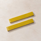Two glossy yellow rectangular ceramic tiles with rounded corners, displayed diagonally on a textured off-white surface.