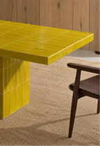 Glossy citron citron yellow rectangular ceramic tiles covering a dining table, paired with a dark wood chair and natural woven rug.