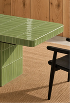 
Glossy sage green rectangular ceramic tiles covering a dining table, paired with a dark wood chair and natural woven rug.
