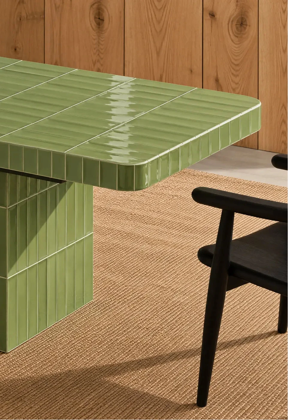 
Glossy sage green rectangular ceramic tiles covering a dining table, paired with a dark wood chair and natural woven rug.
