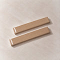 Two rectangular beige wall-mounted hooks with a glossy finish, displayed diagonally on a textured beige background.