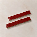 Two glossy red rectangular ceramic tiles with rounded corners, arranged diagonally on a textured beige background.