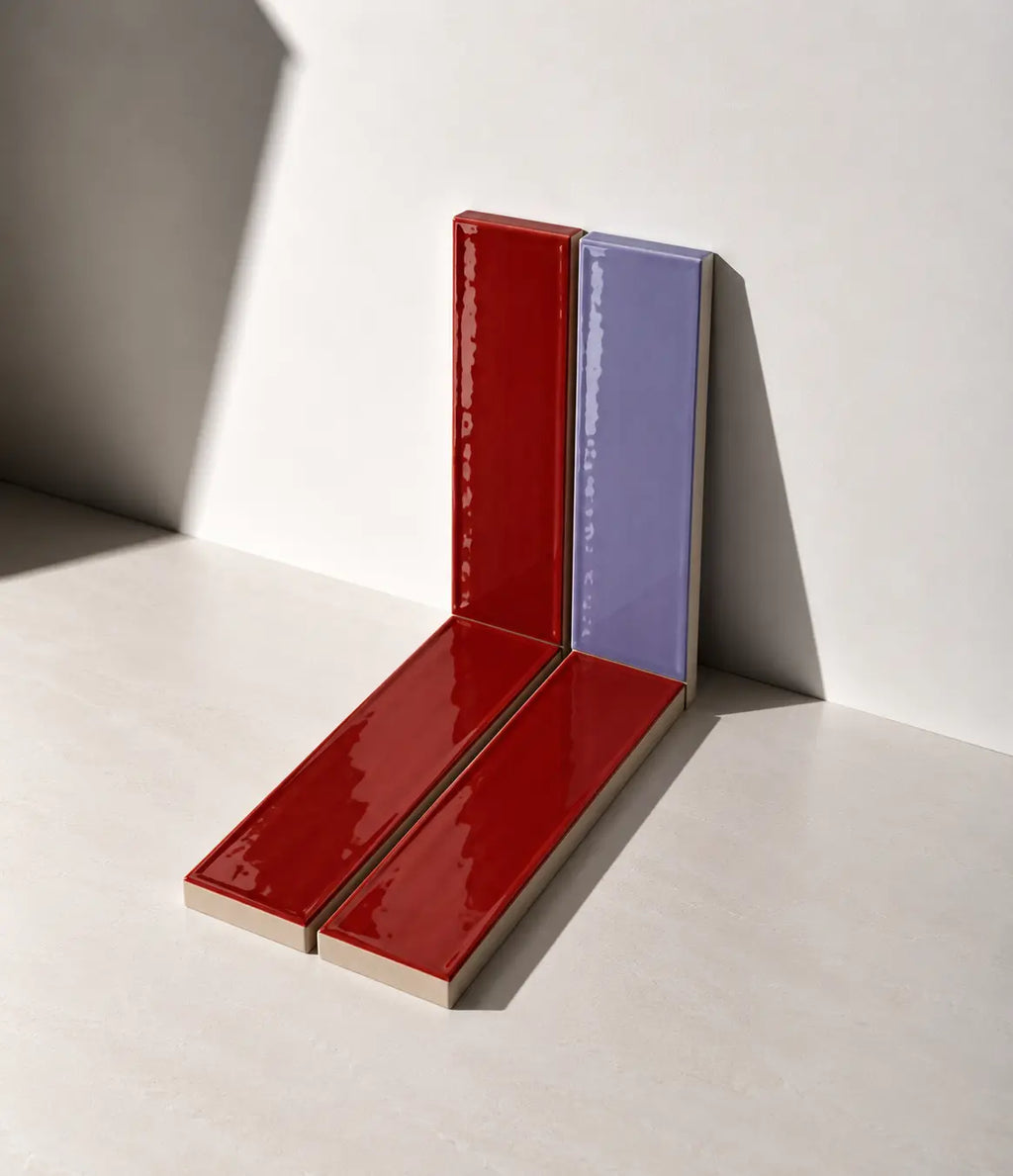 Glossy Scarlet Red and Lilac handmade ceramic tiles arranged against a white wall in natural sunlight.