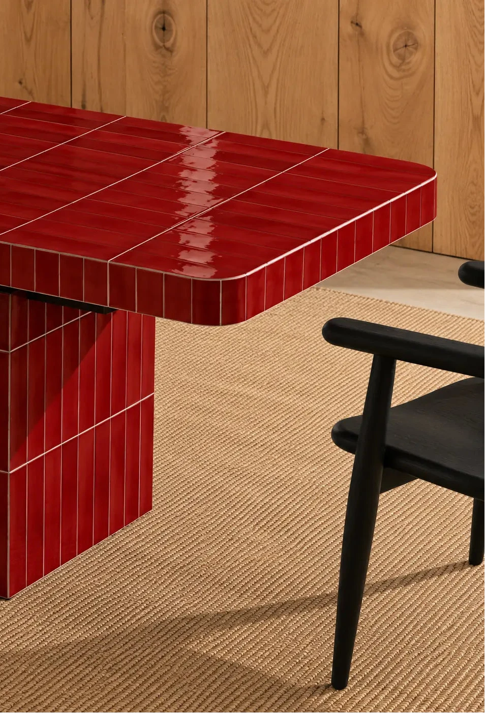 
Glossy scarlet red rectangular ceramic tiles covering a dining table, paired with a dark wood chair and natural woven rug.