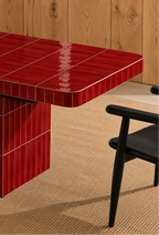 
Glossy scarlet red rectangular ceramic tiles covering a dining table, paired with a dark wood chair and natural woven rug.