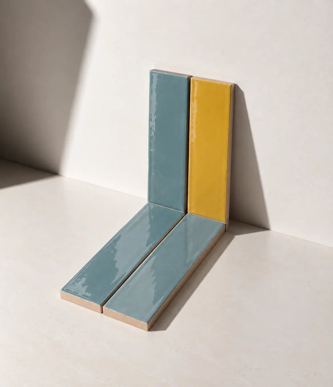 Glossy Saffron Yellow and Sky Blue handmade ceramic tiles arranged against a white wall in natural sunlight.
