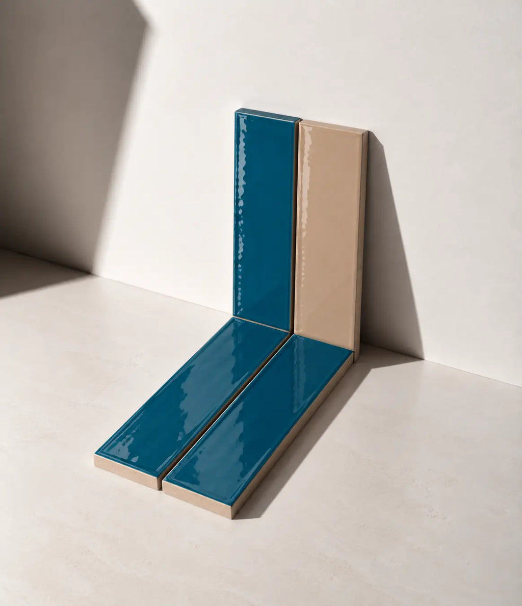 Glossy Teal Blue and Sand colours handmade ceramic tiles arranged against a white wall in natural sunlight.