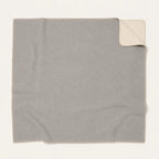 A square light gray throw blanket with a cream-colored underside, shown flat on a white background with one corner folded over.