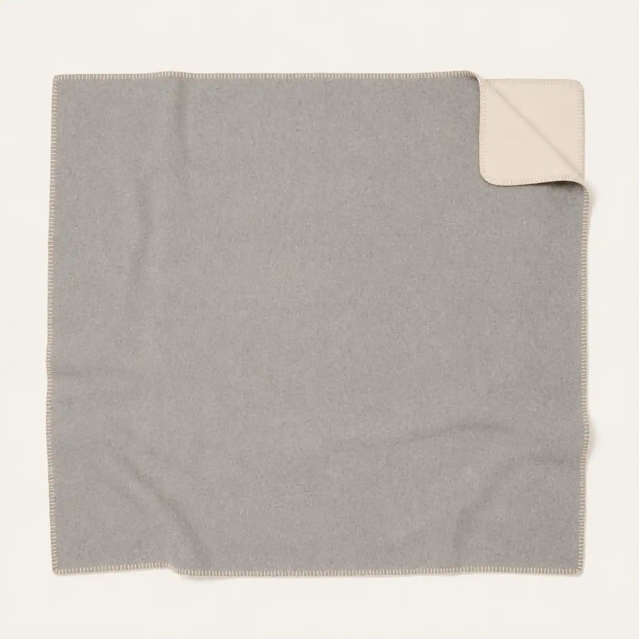 A square light gray throw blanket with a cream-colored underside, shown flat on a white background with one corner folded over.