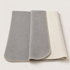 A folded gray throw blanket with a cream-colored reverse side and matching cream stitched border, displayed on a light off-white background.
