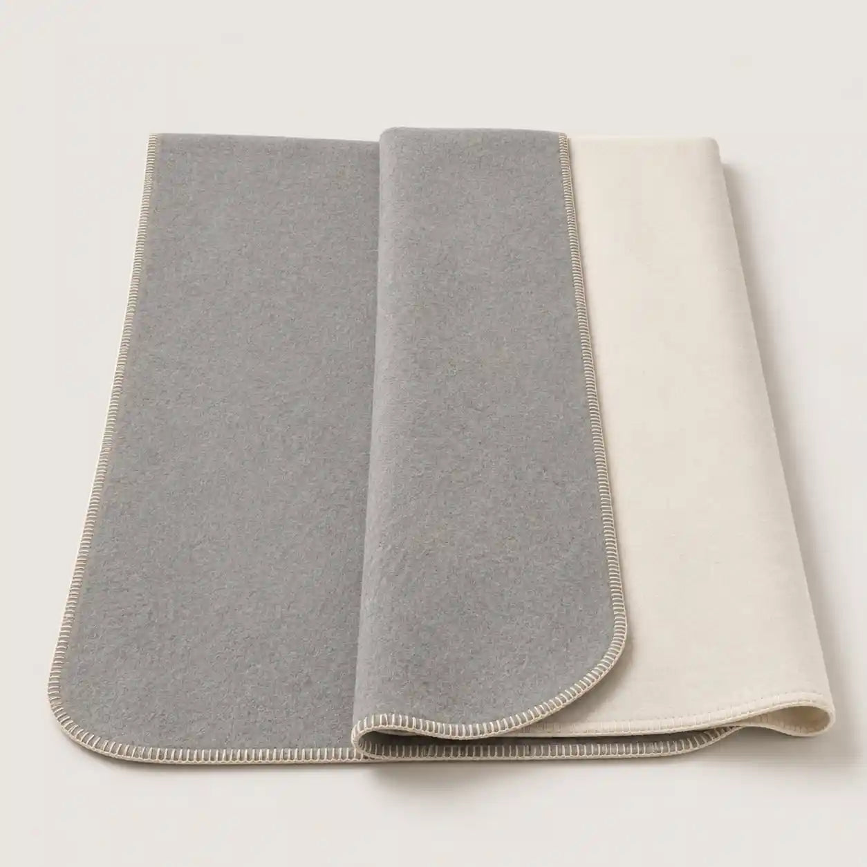 A folded gray throw blanket with a cream-colored reverse side and matching cream stitched border, displayed on a light off-white background.