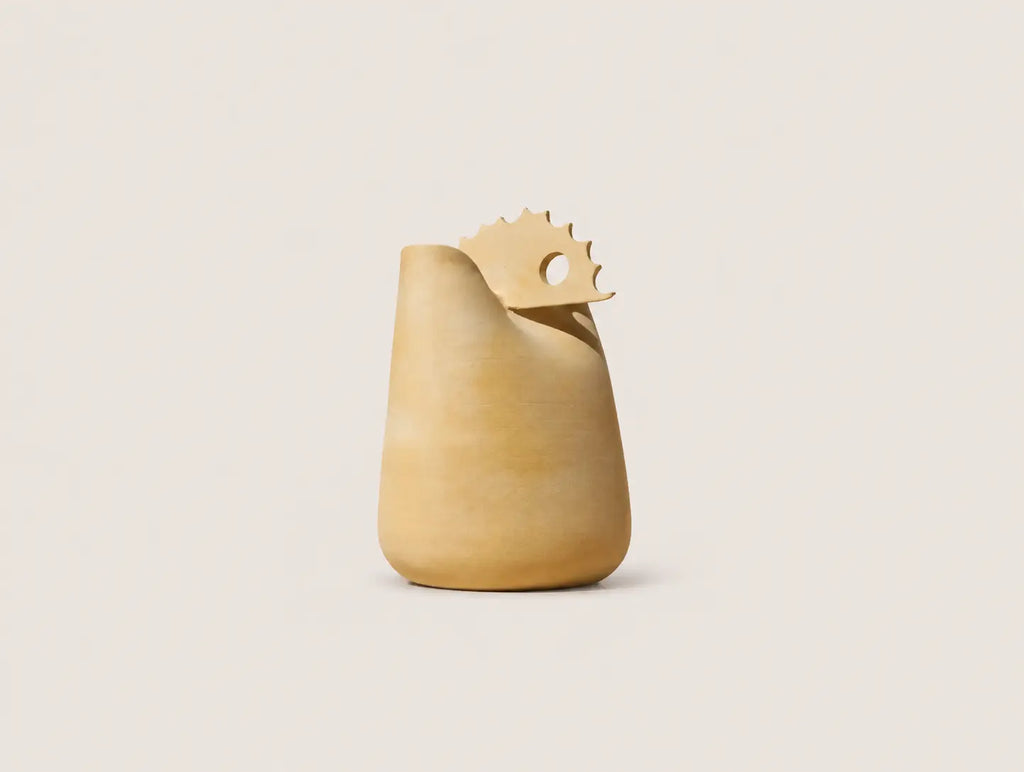A sculptural ceramic pitcher or vase in a warm sandy beige color, featuring a wide flared rim and a decorative serrated tab on top with a circular cutout, set against a solid light beige background.