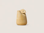 A sculptural ceramic pitcher or vase in a warm sandy beige color, featuring a wide flared rim and a decorative serrated tab on top with a circular cutout, set against a solid light beige background.