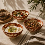Three ceramic snack bowls with different food items on a table with a plant in the background
