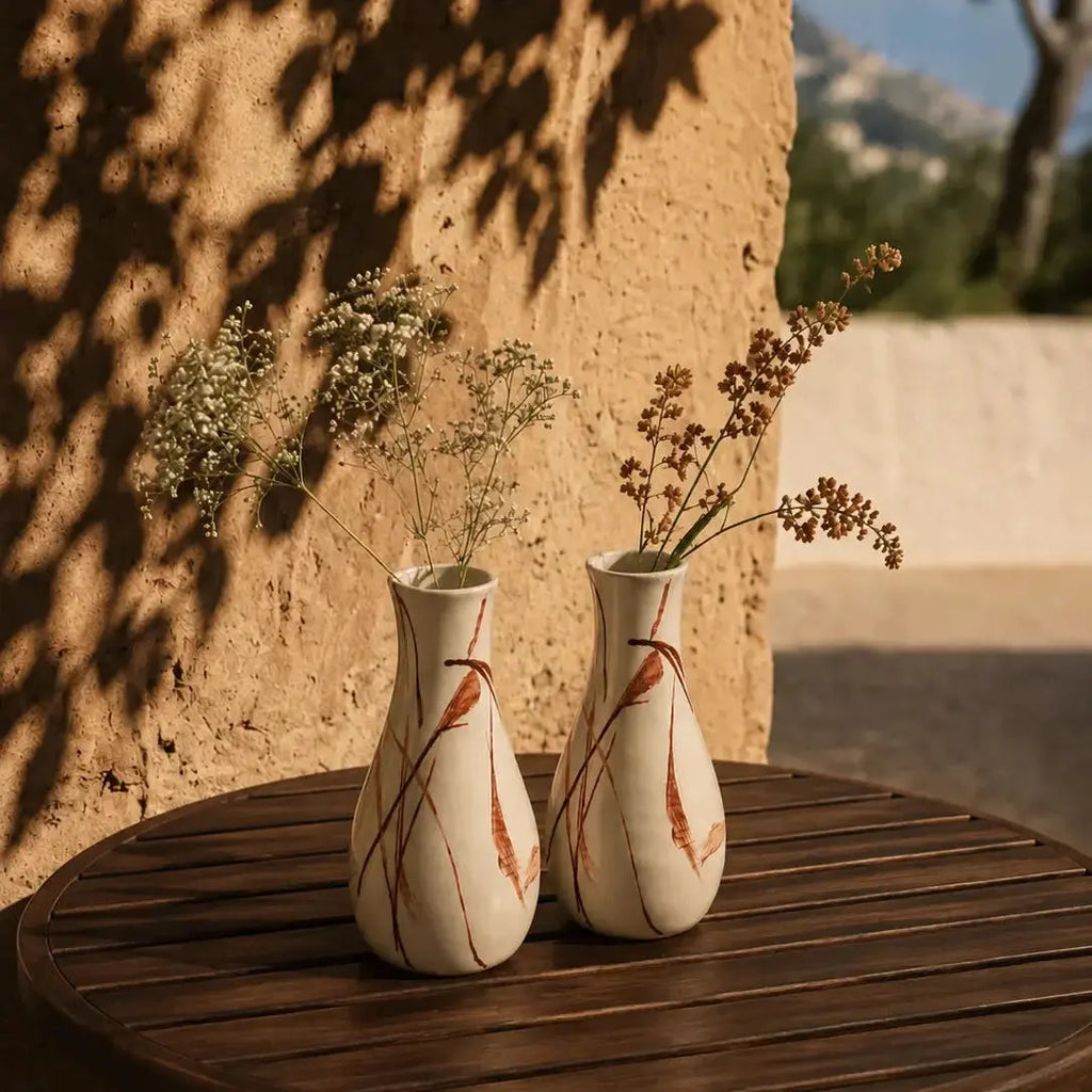 Two decorative vases with floral arrangements on a wooden table against a textured wall.