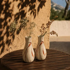 Two decorative vases with floral arrangements on a wooden table against a textured wall.