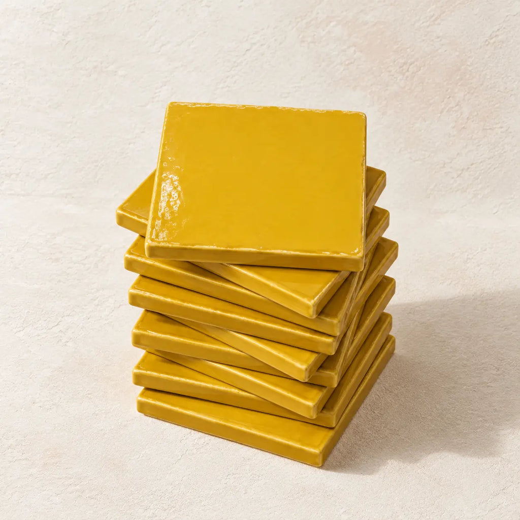 A stack of glossy square yellow coasters on a textured off-white background.