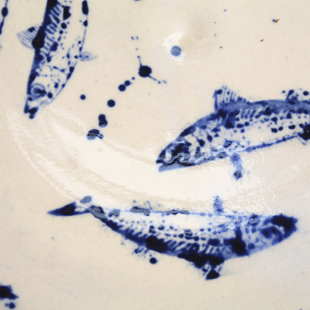 Close-up of blue hand-painted fish illustrations and splatter details on a handcrafted ceramic plate.