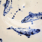 Close-up of blue hand-painted fish illustrations and splatter details on a handcrafted ceramic plate.