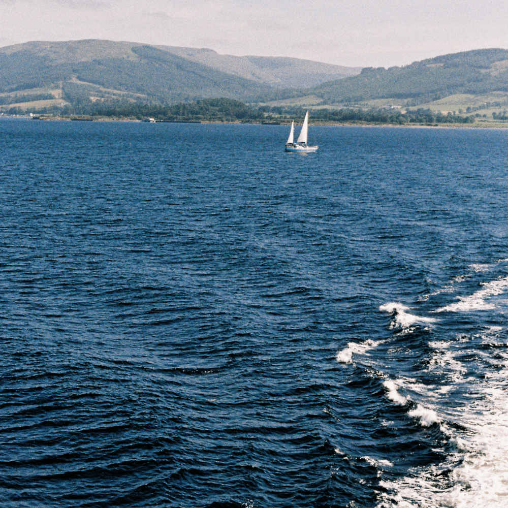 A sailboat on a deep blue sea with distant green hills in the background.
