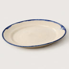 A round ceramic plate with a warm cream interior and a rustic, hand-painted dark blue rim, shown on a light gray background.