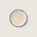 A small round ceramic side plate with a cream-colored interior and a hand-painted blue rim, shown from a top-down view on a light off-white background.