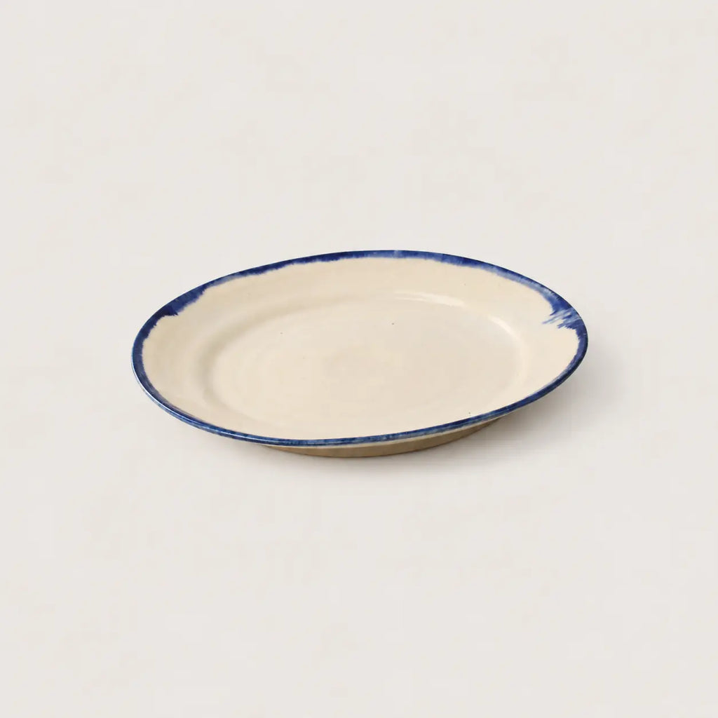 A small oval ceramic plate with a cream-colored glaze and a hand-painted dark blue rim, shown on a plain light background.