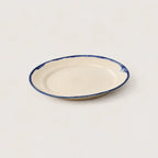 A small oval ceramic plate with a cream-colored glaze and a hand-painted dark blue rim, shown on a plain light background.