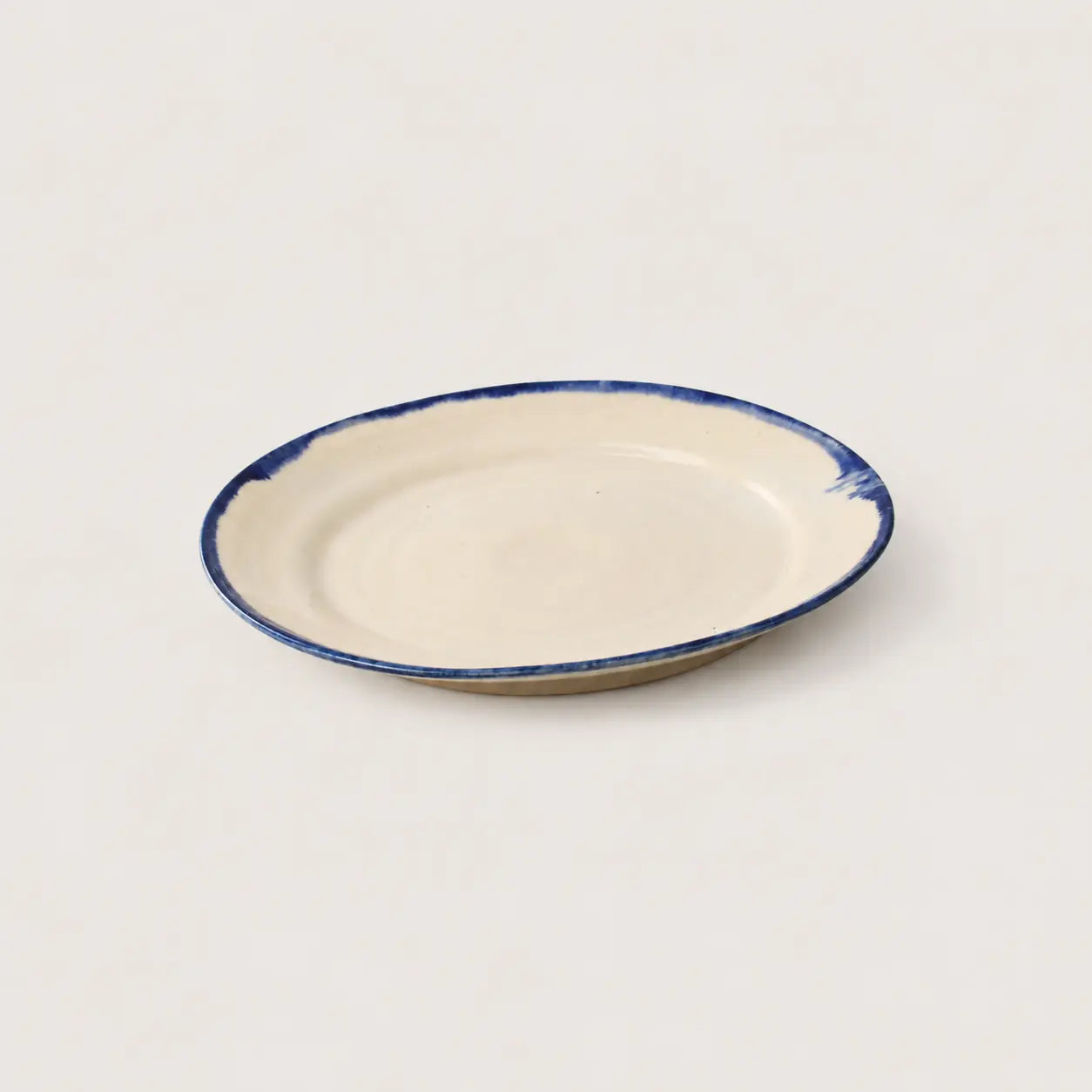 A small oval ceramic plate with a cream-colored glaze and a hand-painted dark blue rim, shown on a plain light background.