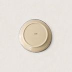 The underside of a round ceramic side plate or dish, showing a cream-coloured glaze with a thin dark blue rim and a small printed brand mark in the centre, set against a plain off-white background.