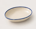 An oval ceramic soup bowl with a glossy off-white interior and a textured, hand-painted dark blue rim, shown on a neutral light gray background.