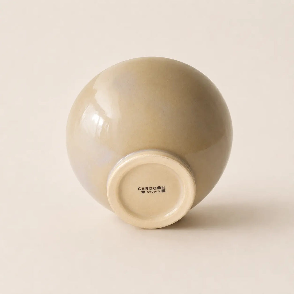 A glossy ceramic soup bowl with a rounded, dome-like shape, shown from its base. The bowl has a warm beige-gray glazed exterior and a cream-coloured unglazed base with the brand name 'CARDOON STUDIO' visible.