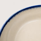 Close-up of a ceramic soup bowl a warm off-white interior with a dark blue hand-painted brush-stroke rim against a light background.