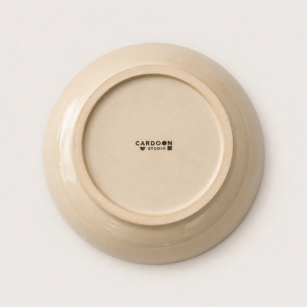 The underside of a round ceramic soup bowl in a warm cream-beige glaze, featuring the black printed brand name 'CARDON STUDIO' in the centre, set against a clean white background.
